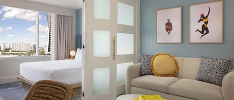 A hotel room with a bed, a sofa, a chair, a coffee table, and two framed artworks on the wall.