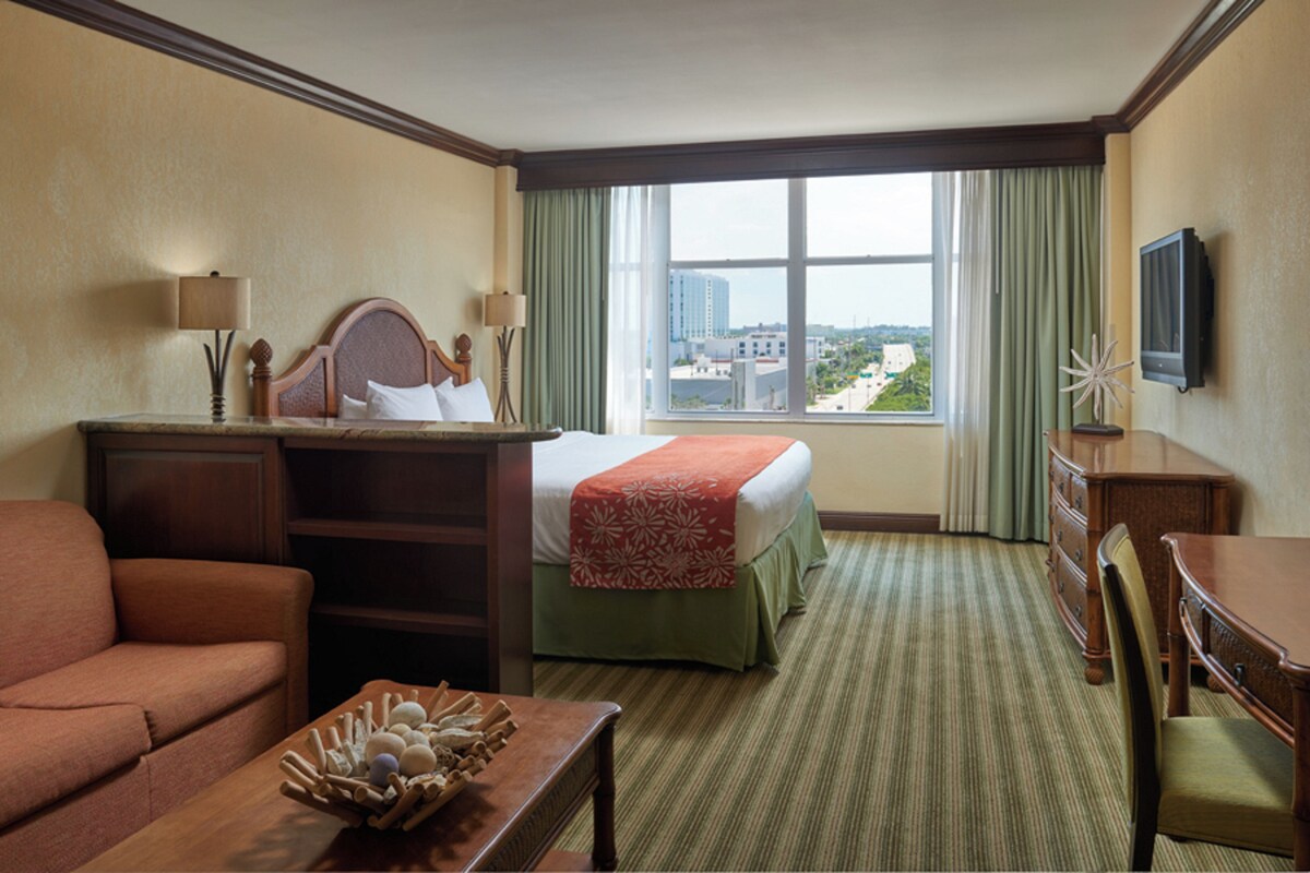 A hotel room with a bed, a desk, a chair, a sofa, and a television.
