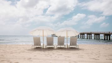 A beach with two white umbrellas and four beach chairs under them, a pier in the background, and the ocean in the distance.
