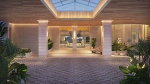 A modern building entrance with a geometric tile floor, large columns, and a skylight. - The Sunny (Sunny Isles Beach)