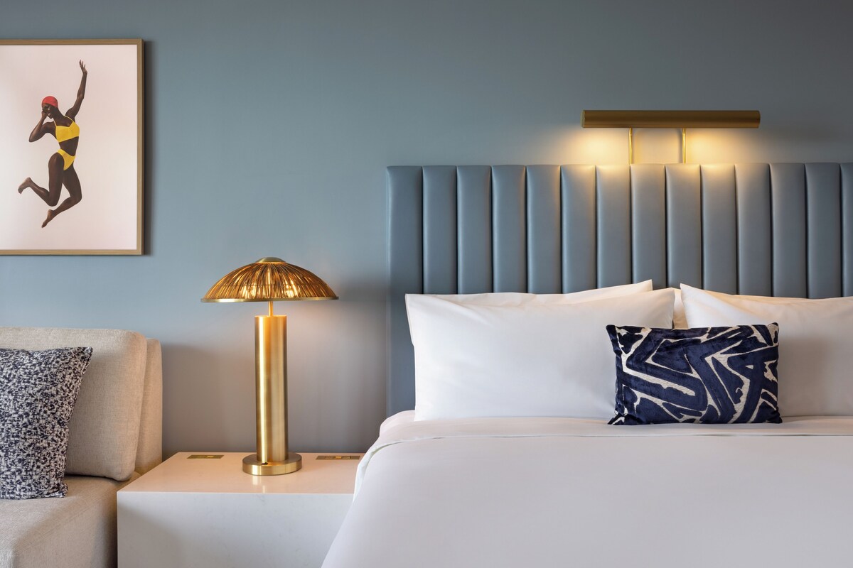 A hotel room with a bed, a nightstand, a lamp, and a framed picture on the wall.