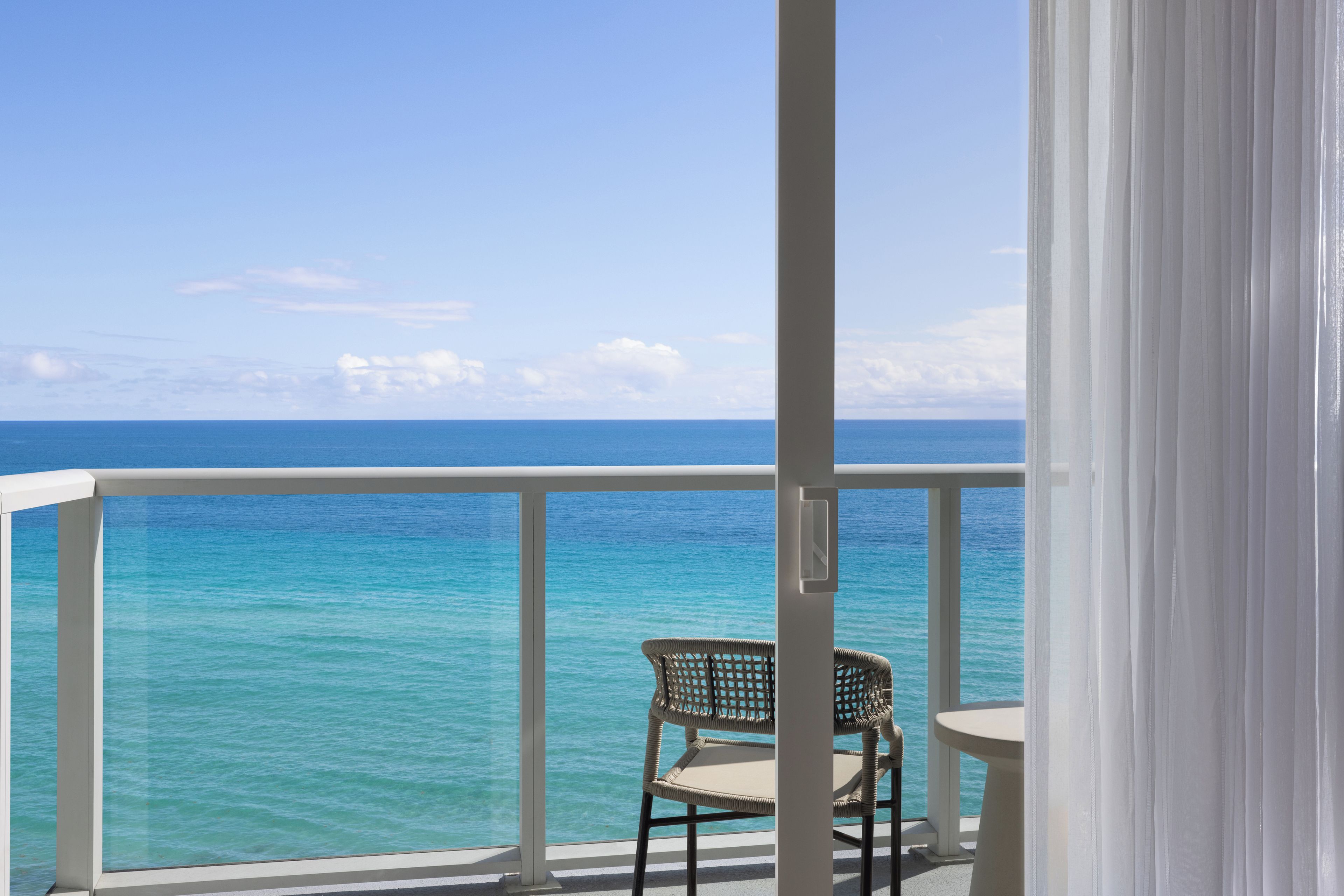 A balcony with a view of the ocean, a wicker chair, and a small table.