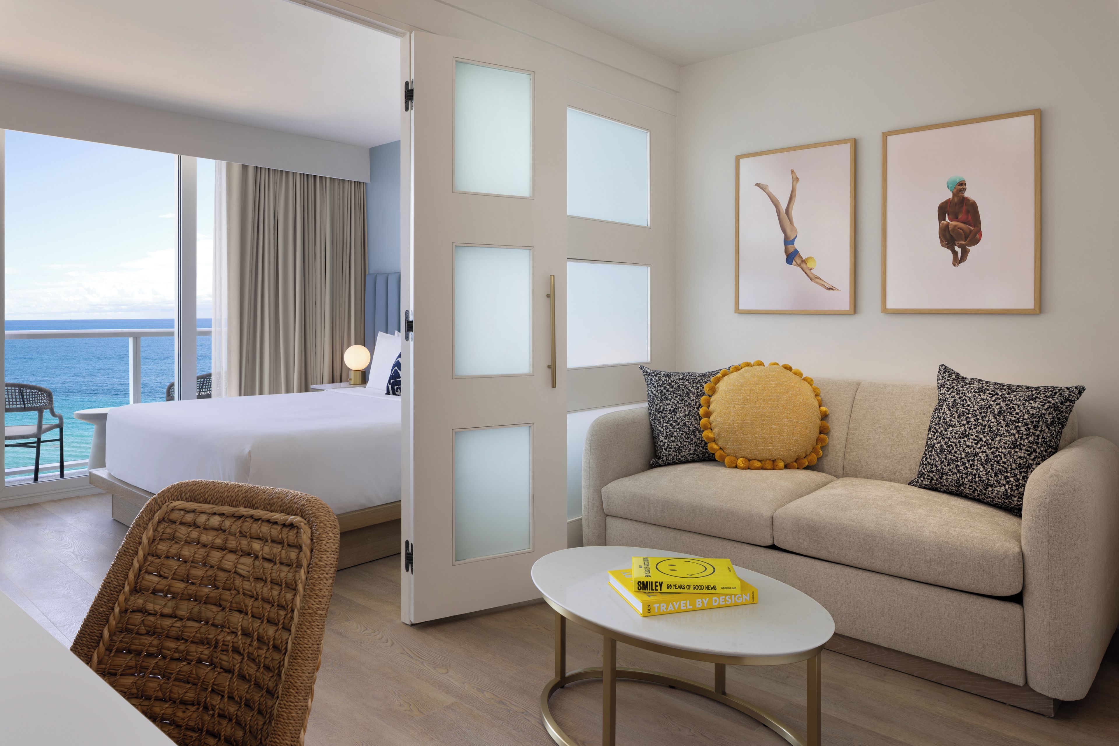 A hotel room with a balcony, a bed, a sofa, a coffee table, and two framed pictures on the wall.