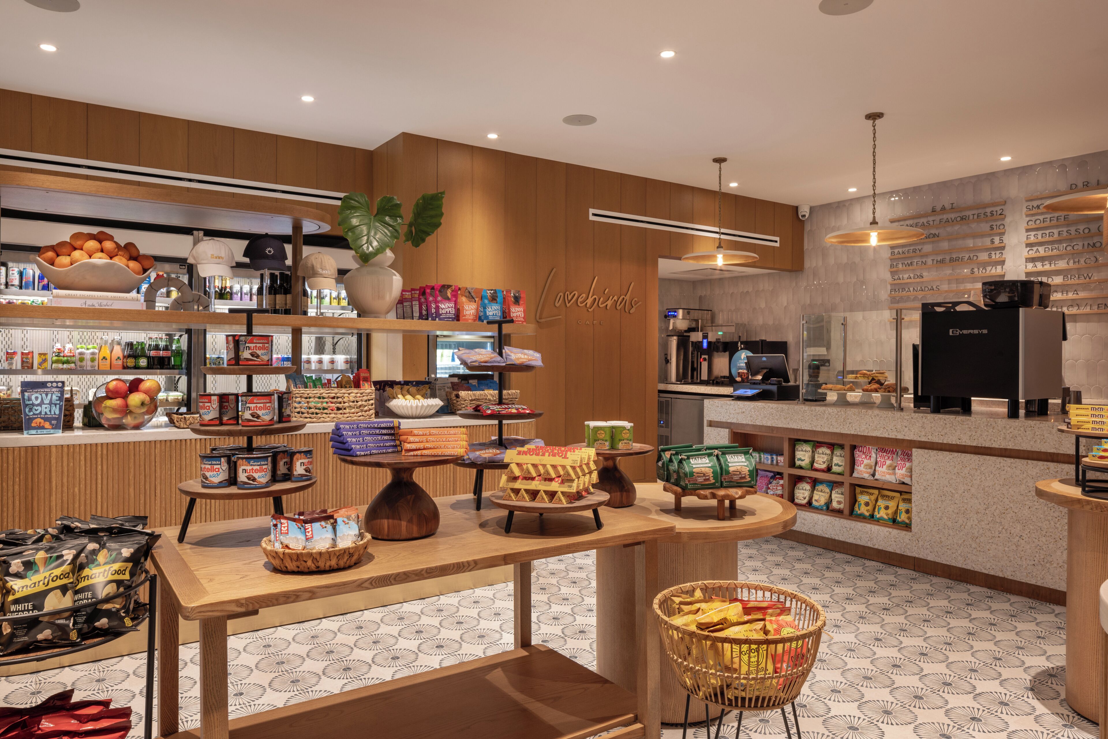 Cafetería con interior de madera, una máquina de café y diferentes alimentos expuestos en las mesas.