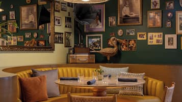 A room with a round table, yellow cushioned seating, and a wall adorned with framed photographs and a large mirror.