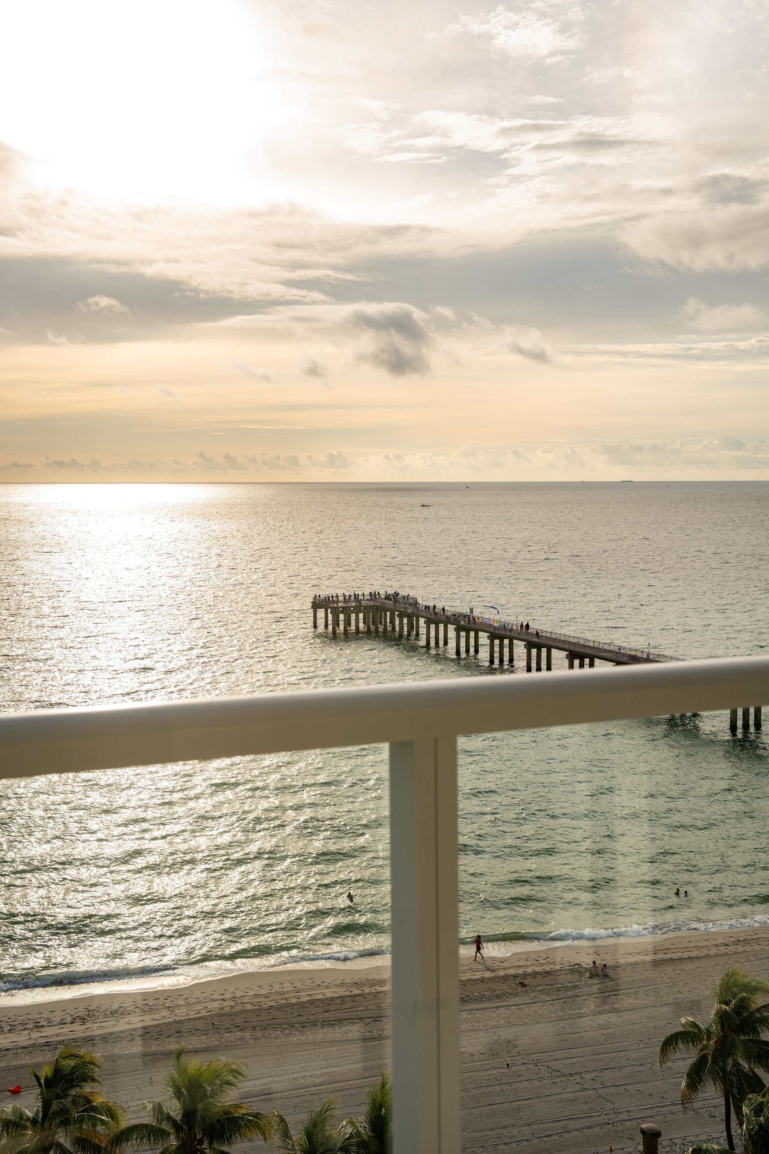 A beach with a pier extending into the water, palm trees, and a clear sky.