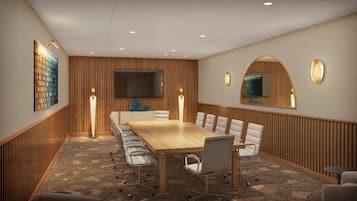 A conference room with a wooden table, white chairs, a large flat-screen TV, and two wall-mounted mirrors.