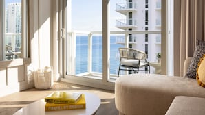 A modern living room with a view of the sea, a balcony with a chair, and a stack of books on a coffee table. - The Sunny (Sunny Isles Beach)