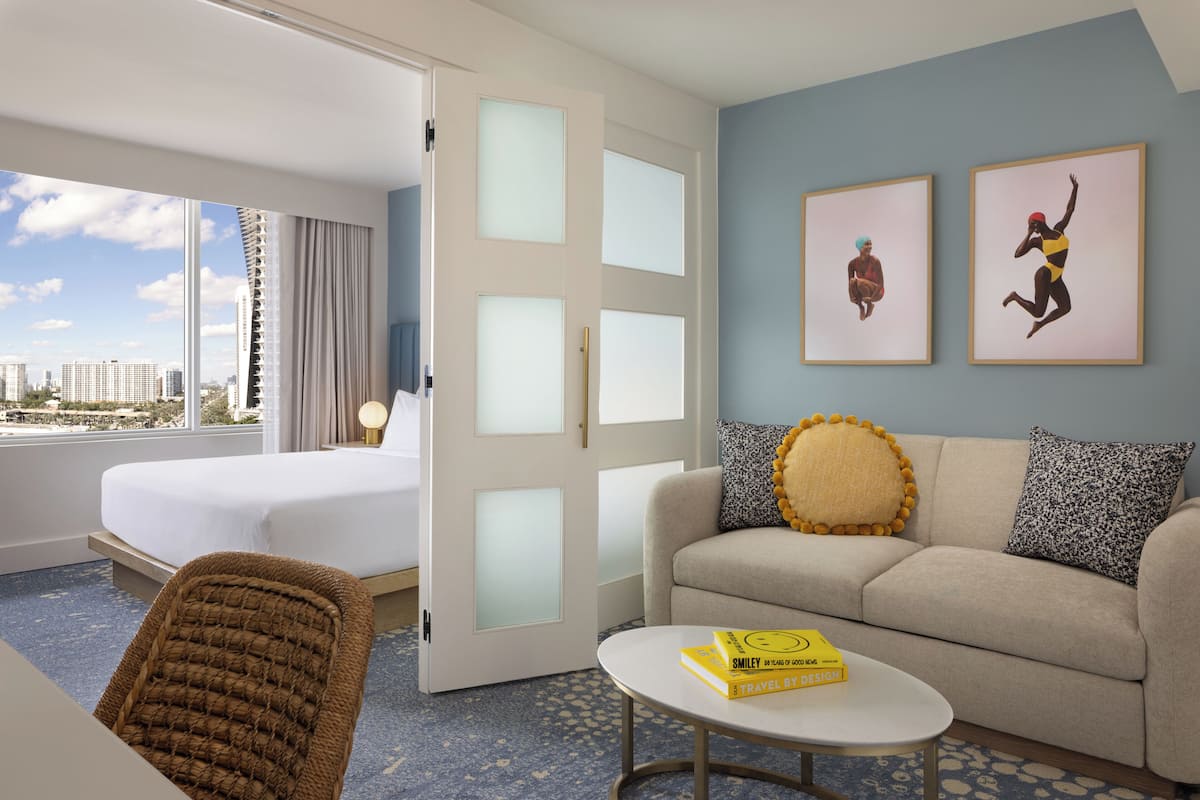 Una habitación de hotel con una cama, un sofá, una silla, una mesita de centro y dos cuadros enmarcados en la pared.