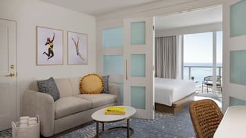 A hotel room with a sofa, a small round table, a bed, and a view of the sea through large windows.