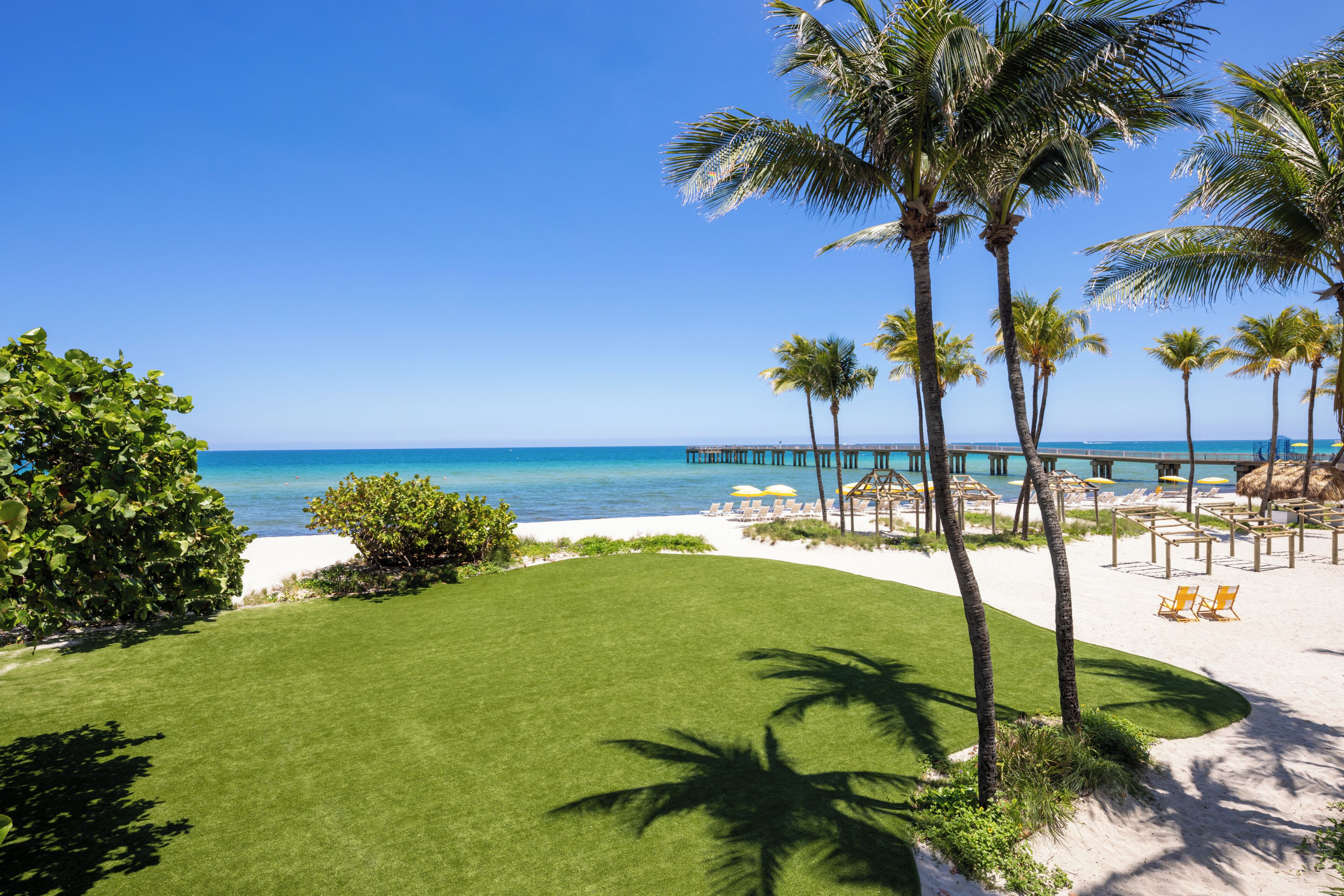 A beach view with palm trees, a pier, and beach chairs.