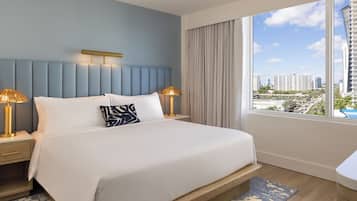 Habitación de hotel con una cama grande, dos lámparas de noche, vista a la ciudad y un ventanal con cortinas.