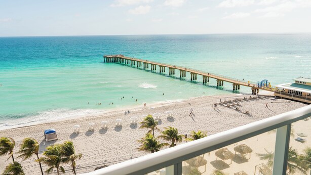 A beach with a pier extending into the ocean, a sandy beach, and palm trees. - The Sunny (Sunny Isles Beach)
