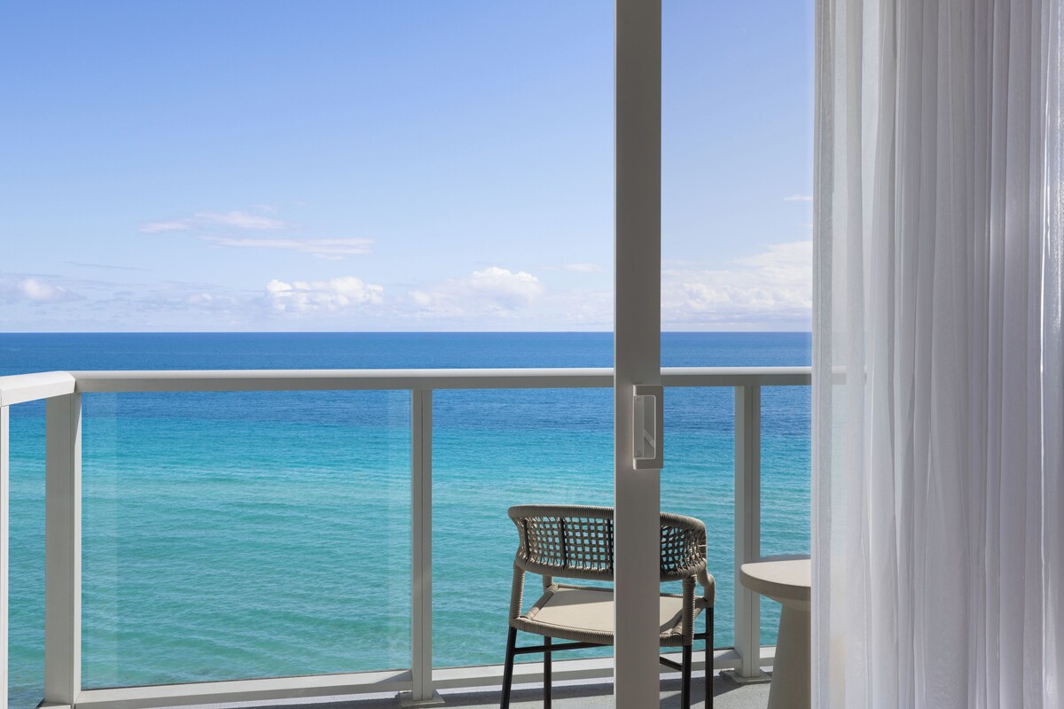 A balcony with a view of the ocean, a wicker chair, and a small table.