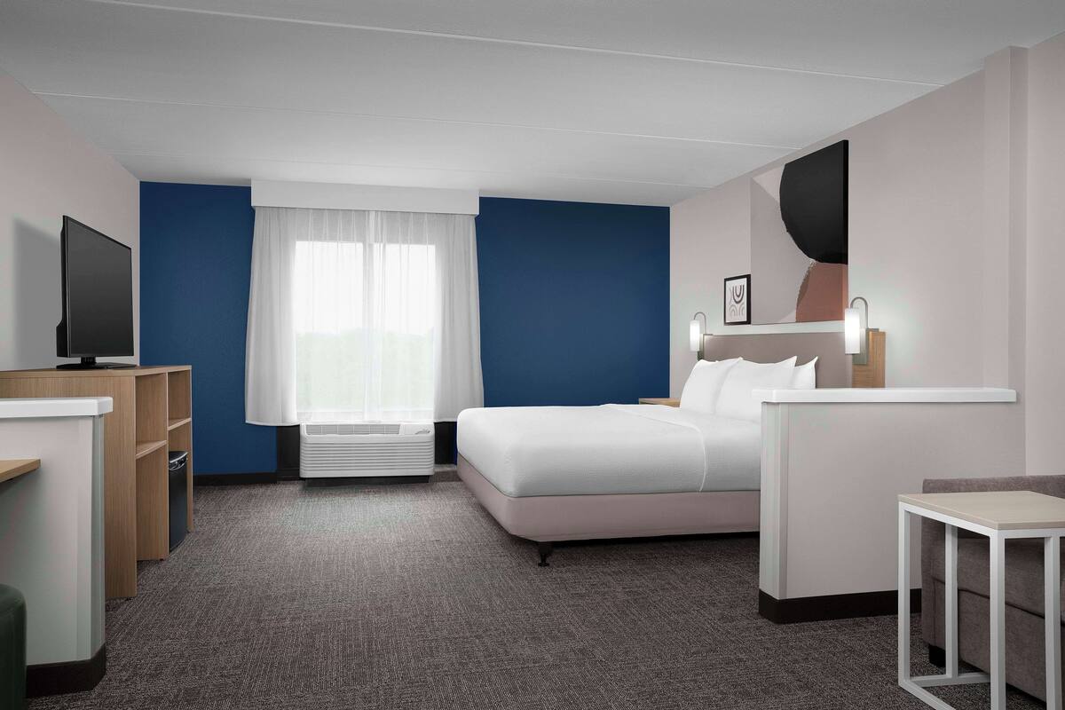 Une chambre d’hôtel avec un lit, un bureau, une chaise, une télévision et une fenêtre avec des rideaux.