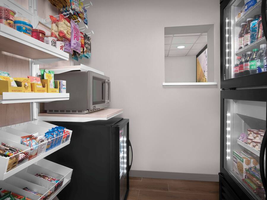 A compact kitchenette with shelves stocked with snacks, a microwave, and a refrigerator.