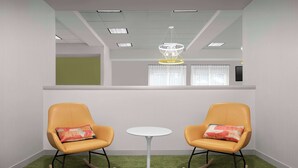 A room with two rocking chairs, a small white table, green carpet, and a ceiling with recessed lighting and a chandelier.