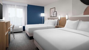 A hotel room with two beds, a desk, a chair, and a large window with curtains.