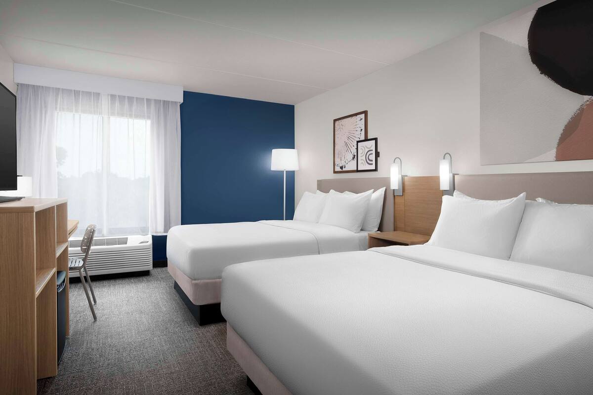 Une chambre d’hôtel avec deux lits, un bureau, une chaise et une grande fenêtre avec des rideaux.