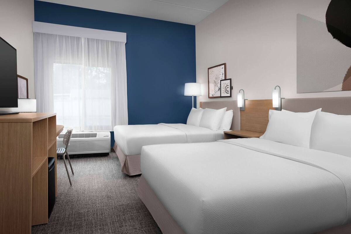 Une chambre d’hôtel avec deux lits, un bureau, une chaise et une fenêtre avec des rideaux.