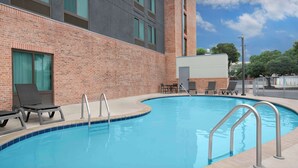A swimming pool with lounge chairs and a brick building in the background.