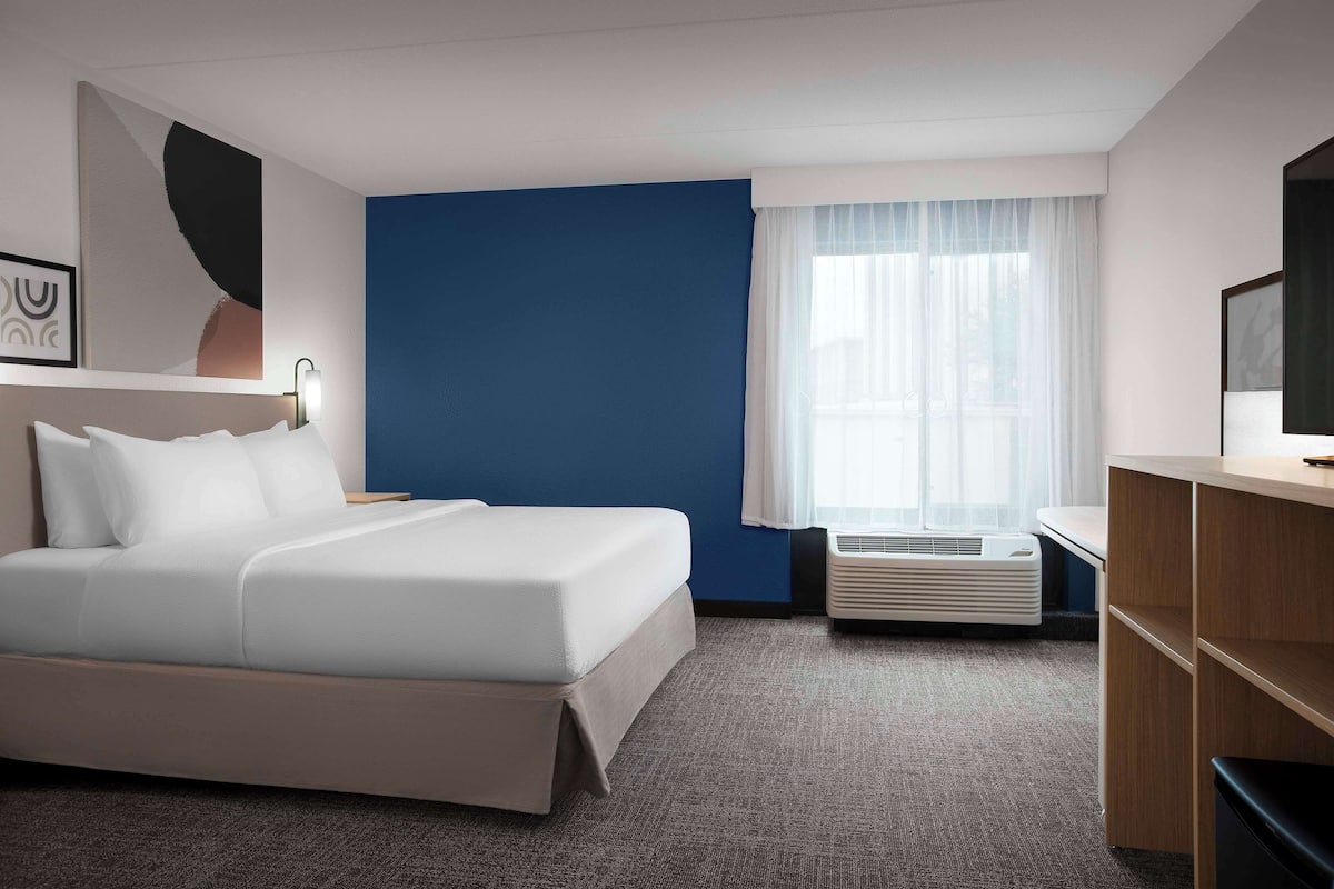 Une chambre d’hôtel avec un lit, un bureau, une télévision et une fenêtre avec des rideaux.