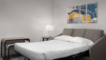Et hotelværelse med en enkelt seng, et natbord, en lampe og et lille bord.