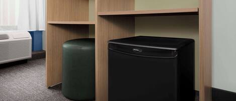 A room with a wooden wardrobe, a green ottoman, and a black trash bin.