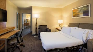 A hotel room with a bed, desk, chair, lamp, and artwork on the wall.