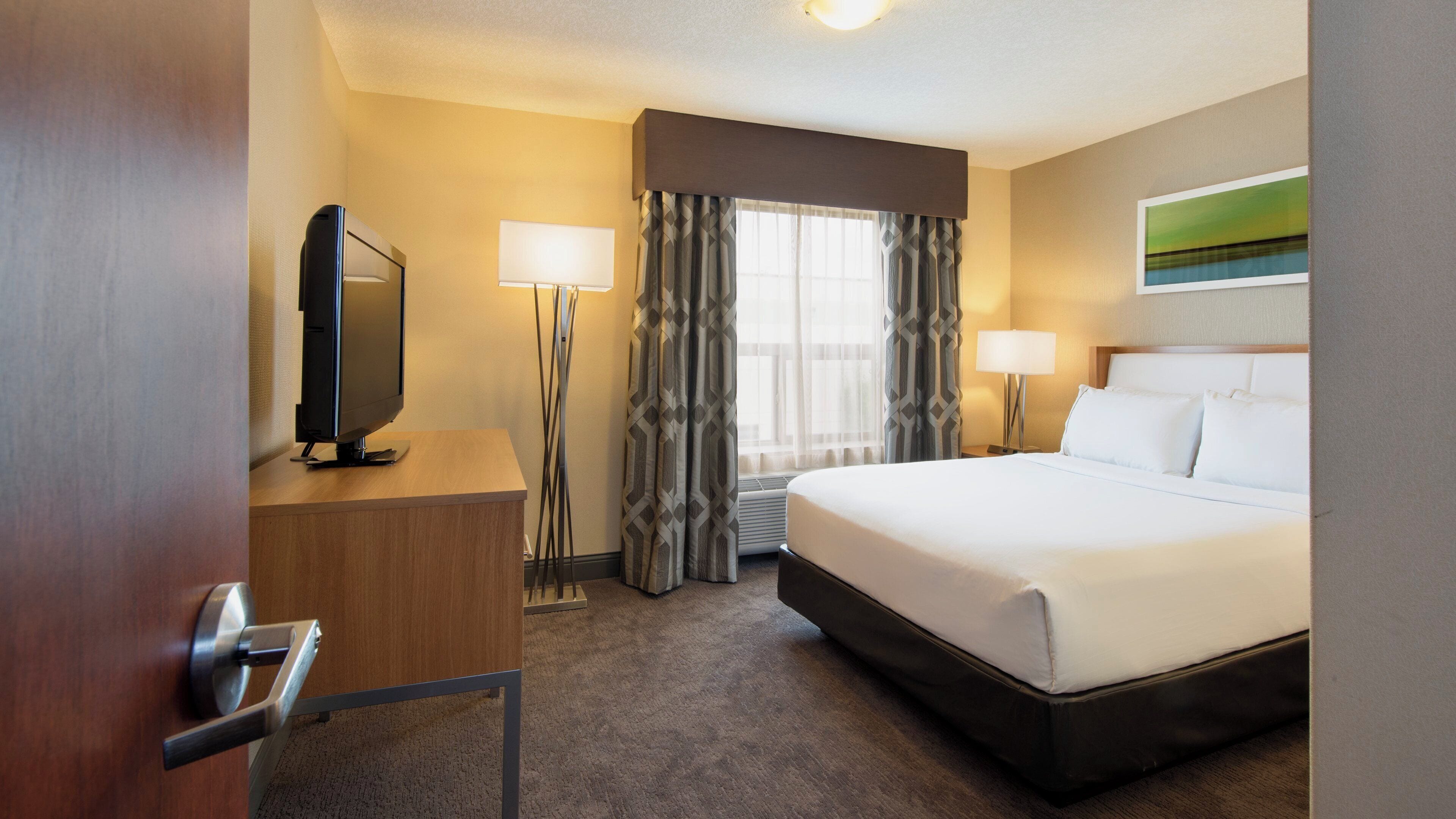 A hotel room with a bed, a desk, a television, a lamp, and a window with curtains.