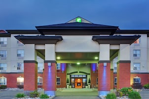 A hotel entrance with a prominent green logo, a covered walkway, and a fire feature in the center.