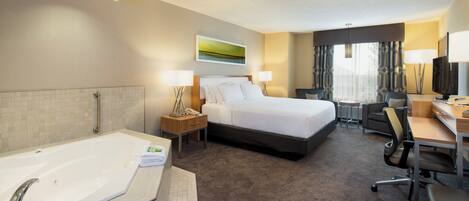 A hotel room with a large bed, a desk, a chair, a desk lamp, a television, and a bathroom with a bathtub and a towel.
