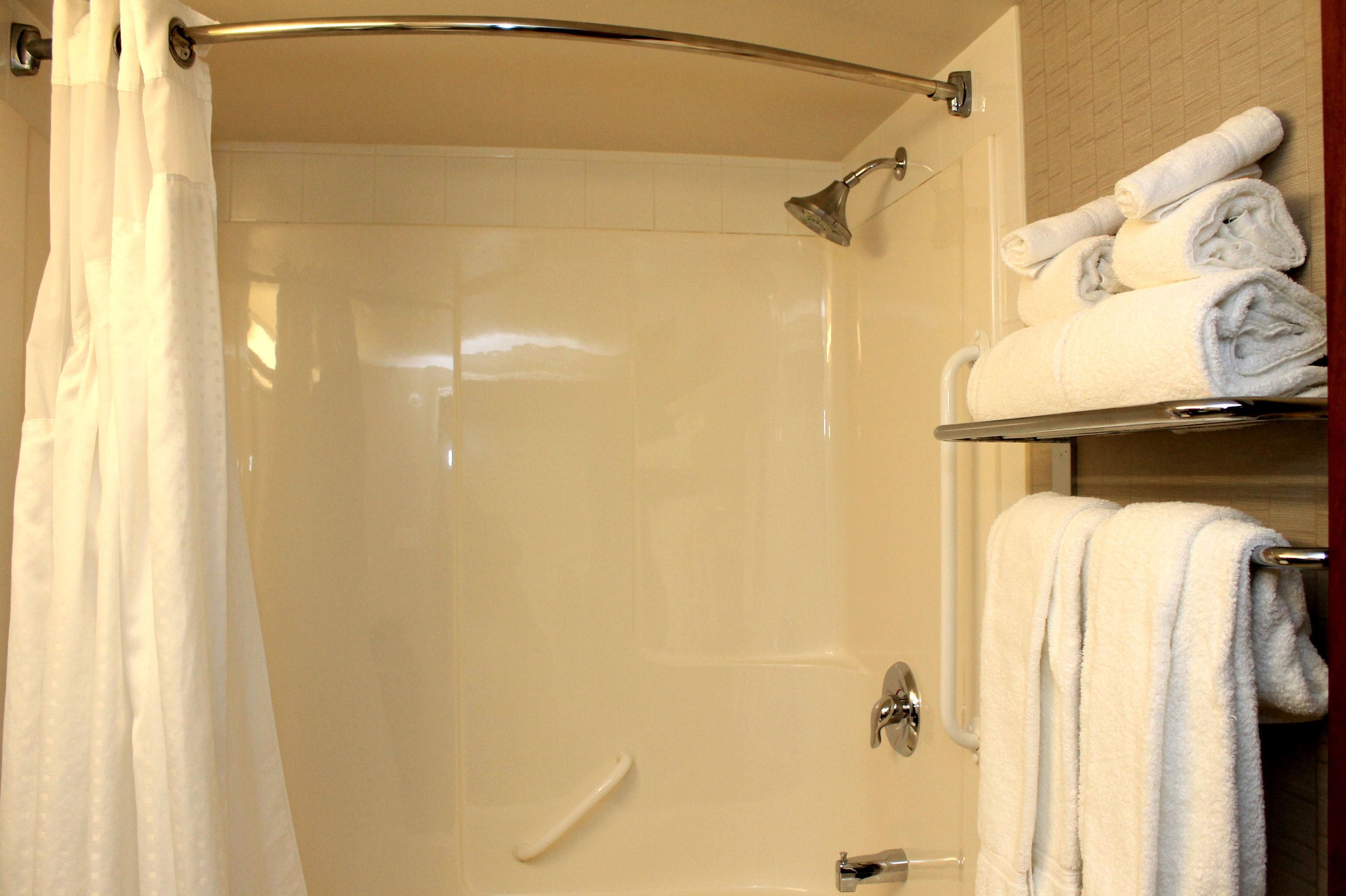 A shower area with a glass door, a towel rack with folded towels, and a showerhead.
