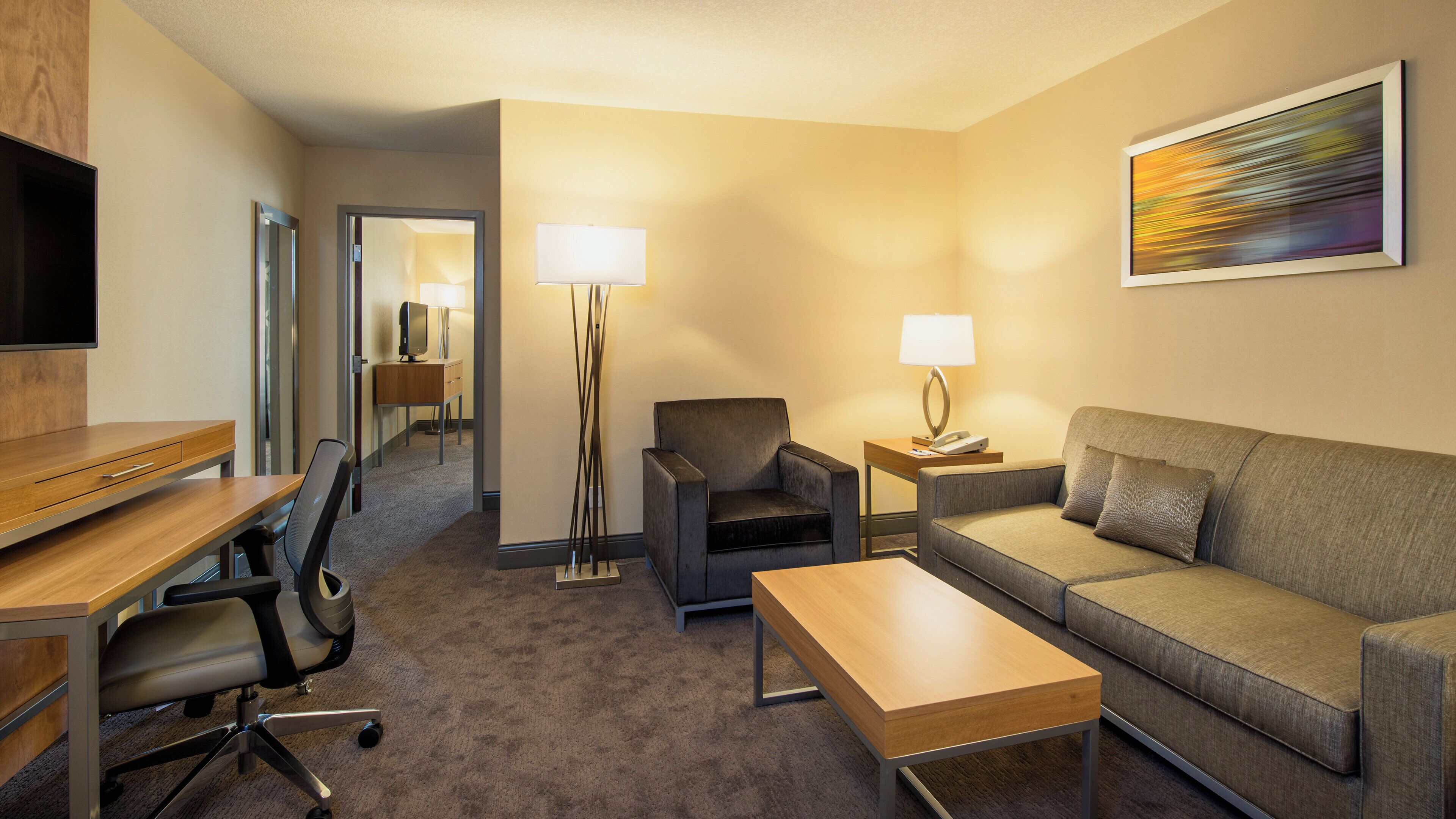 A hotel room with a desk, office chair, sofa, and a flat-screen TV.