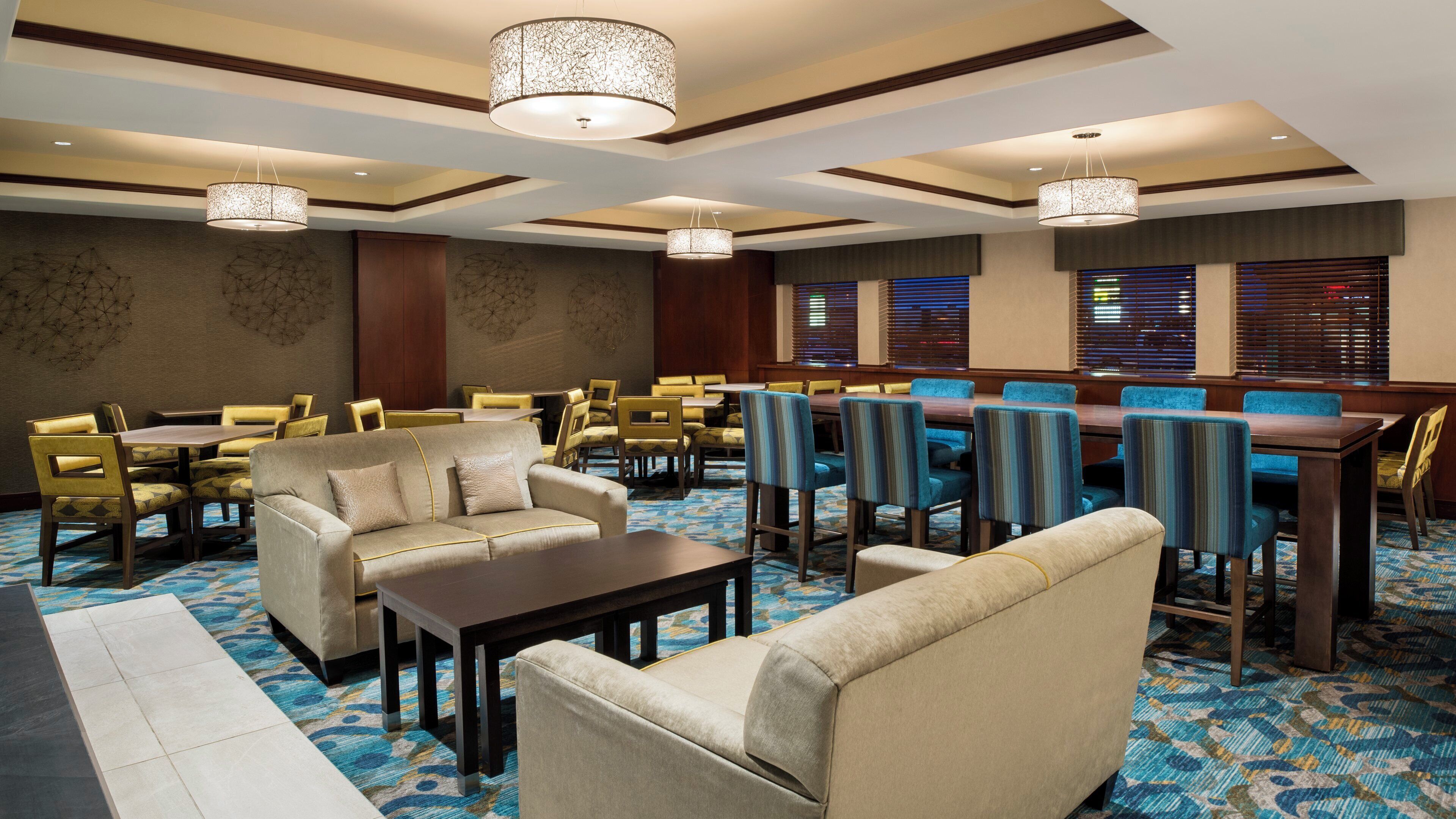 A hotel dining area with multiple tables and chairs, a sofa, and a patterned carpet.