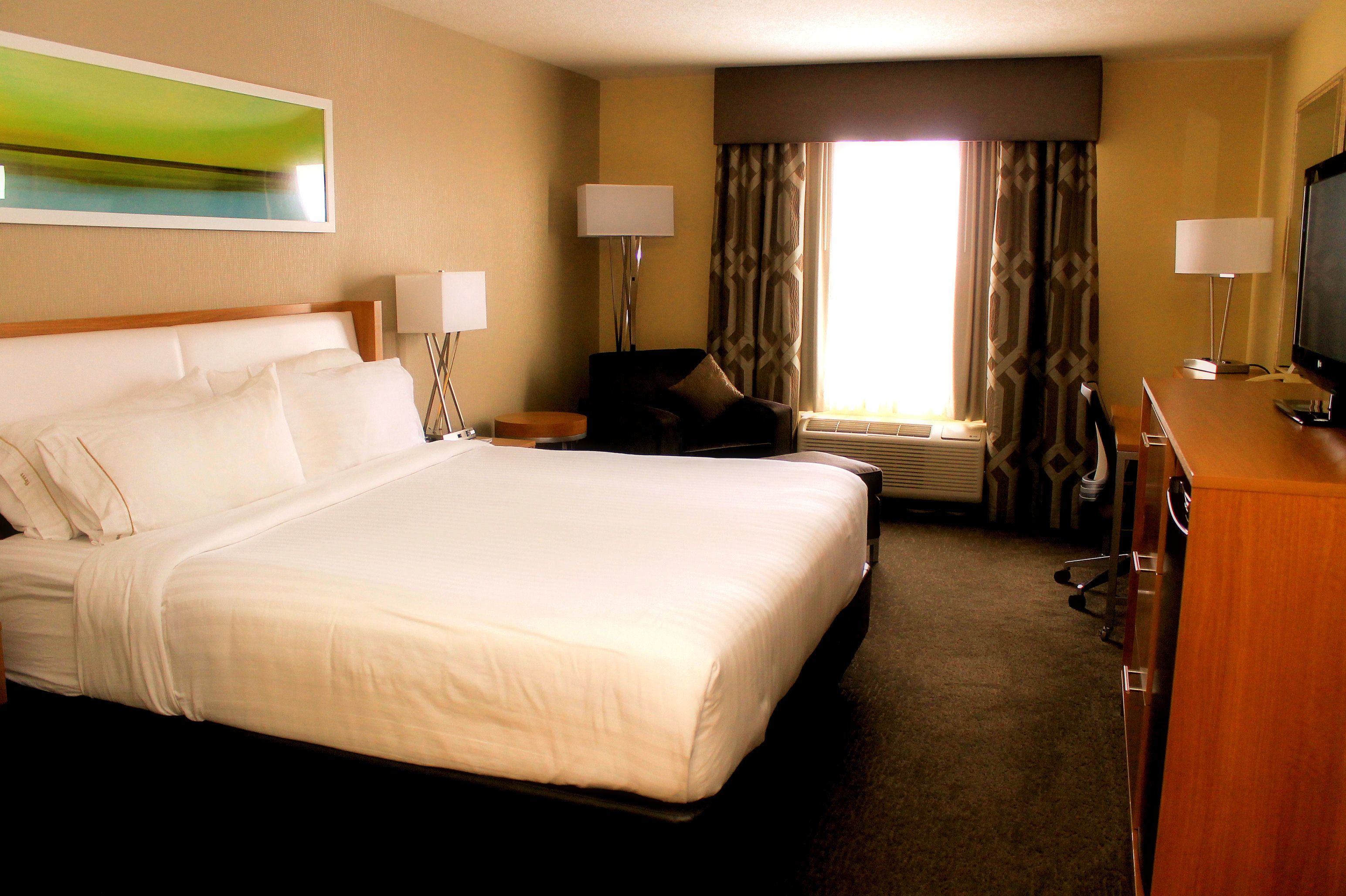 A hotel room with a large bed, a desk with a television, two lamps, and a window with curtains.