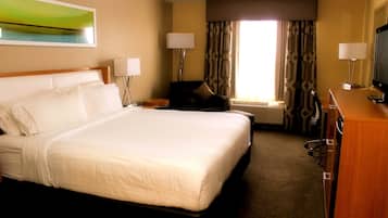 A hotel room with a large bed, a desk with a television, two lamps, and a window with curtains.