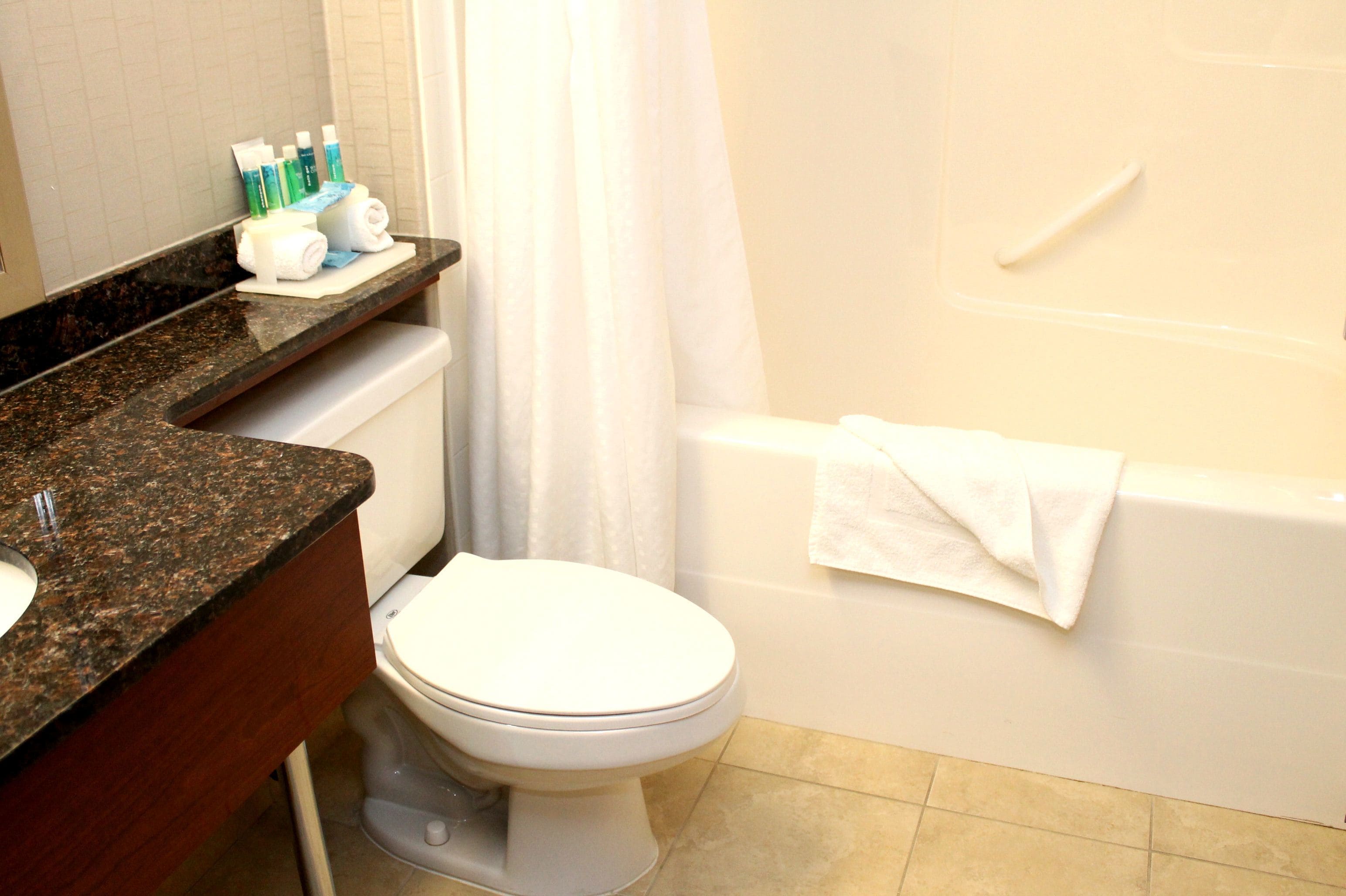 A bathroom with a white toilet, a bathtub with a white towel, and toiletries on the counter.
