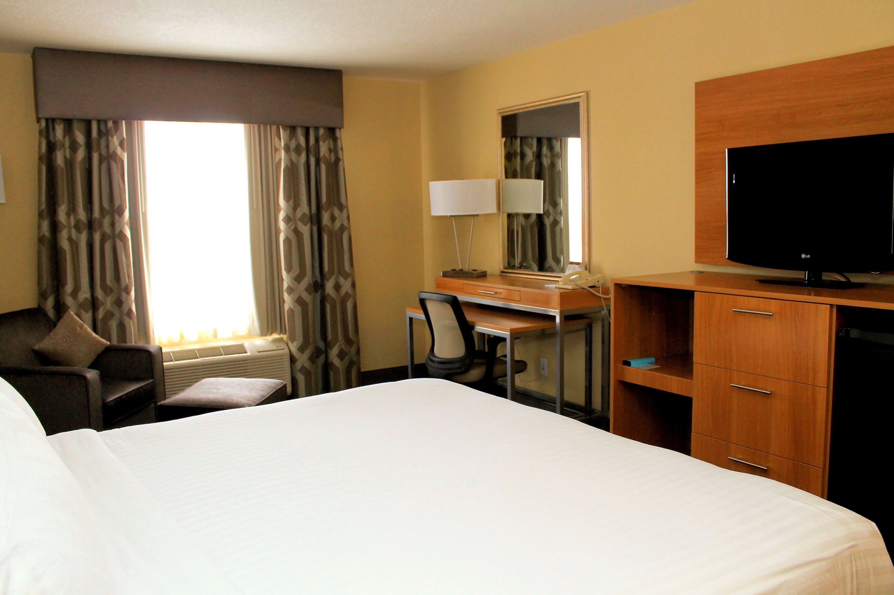 A hotel room with a large bed, a desk with a chair, a television, and a wardrobe.