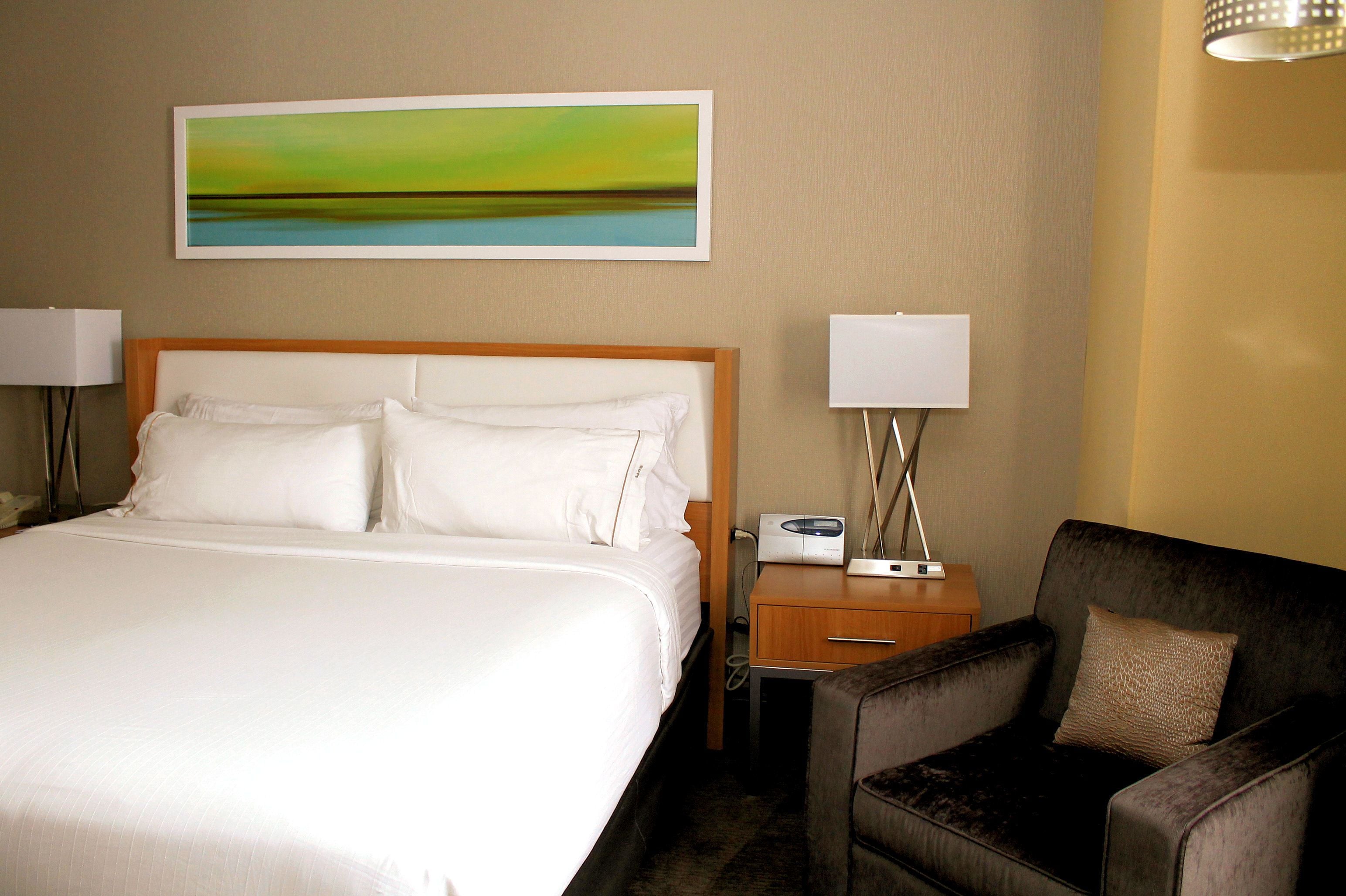 Camera d'albergo con un letto grande, un comodino con una lampada, una sedia e un quadro appeso al muro.