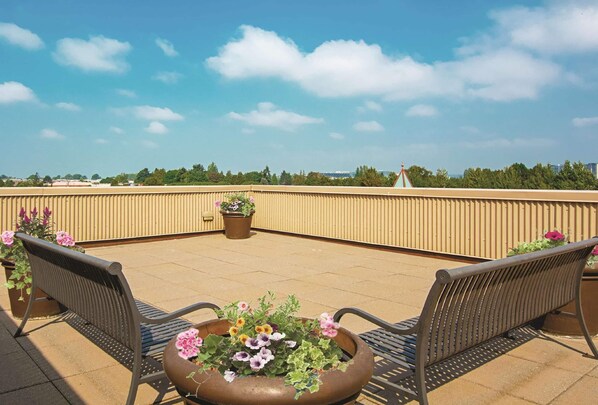 Una terraza en la azotea con dos bancos de metal, una jardinera grande con flores y vistas al horizonte de la ciudad.