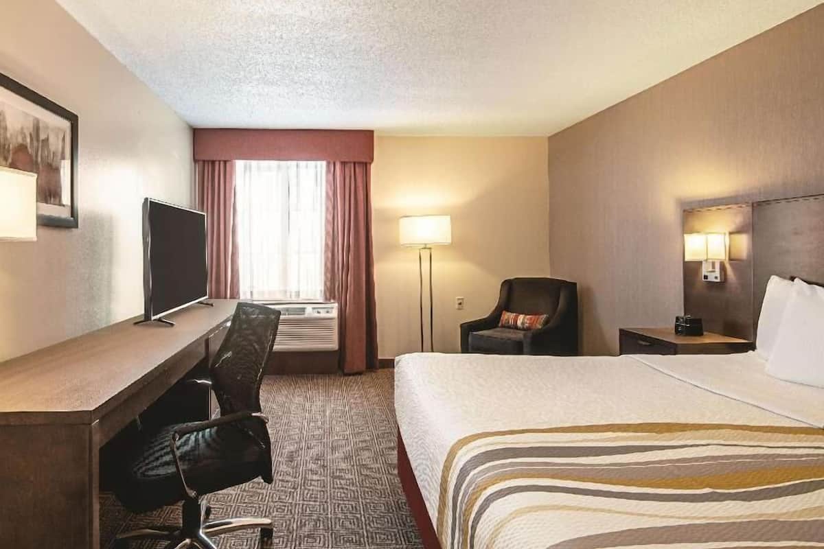 Habitación de hotel con cama, escritorio, silla, televisor, lámpara y aire acondicionado.