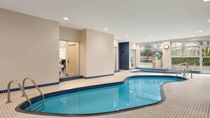 Una piscina con un borde empedrado, una puerta que da a un baño y grandes ventanales con vistas al exterior.