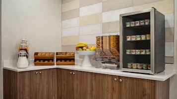 A breakfast bar with a milk pitcher, fruit bowl, bread, and a refrigerated display.