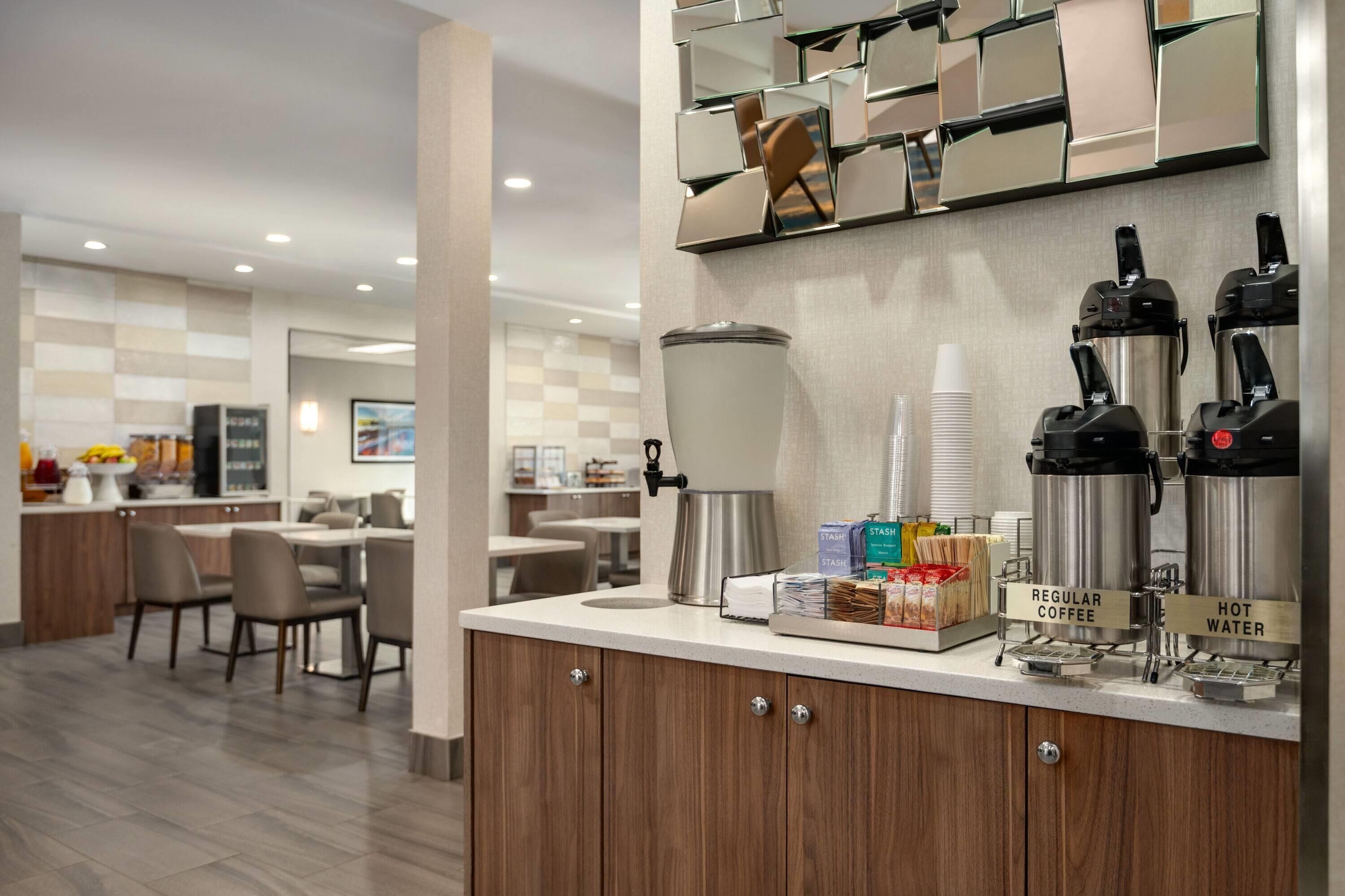 A modern cafe area with a coffee station, seating, and a counter with amenities.