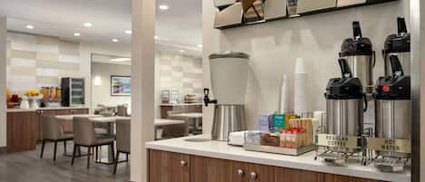 A modern cafe area with a coffee station, seating, and a counter with amenities.