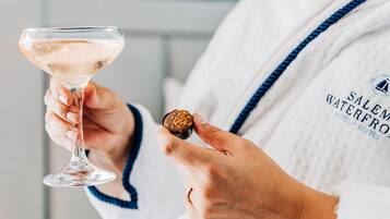 Una persona sosteniendo una copa de martini y un dulce cubierto de chocolate. La persona lleva una bata con la inscripción "Salem Waterfront Hotel".
