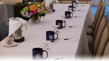 A long table with a white tablecloth, black mugs, and a silver teapot.