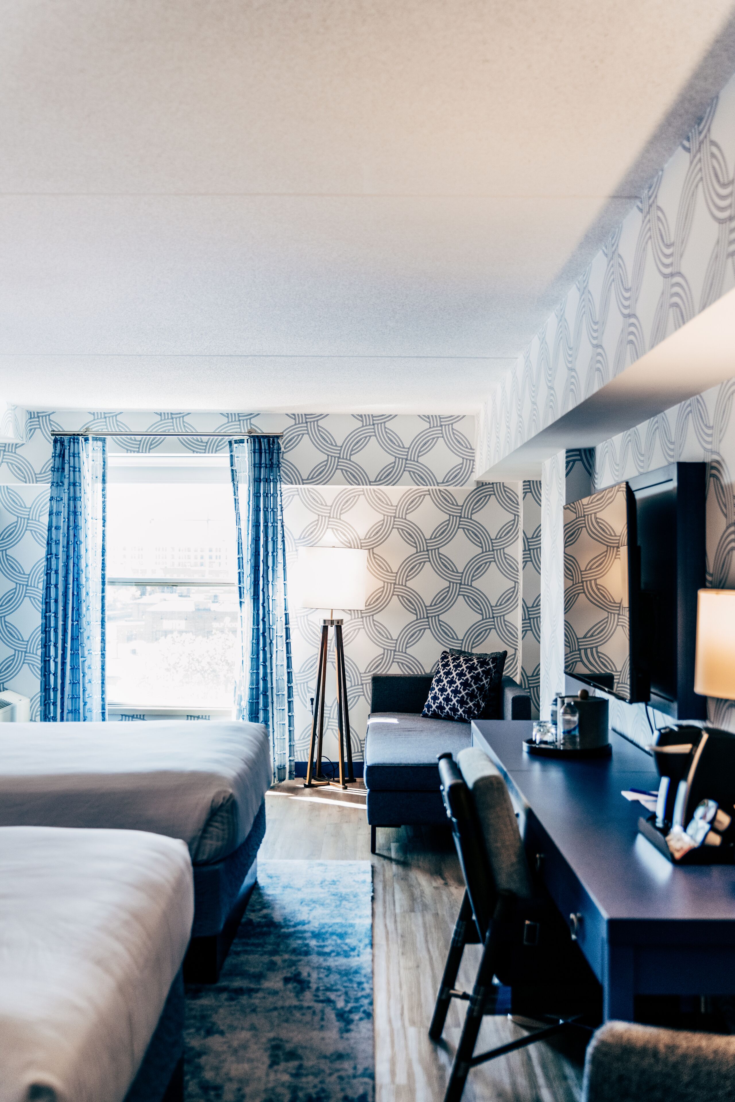 A hotel room with a large bed, a desk with a chair, a television, and a window with curtains.