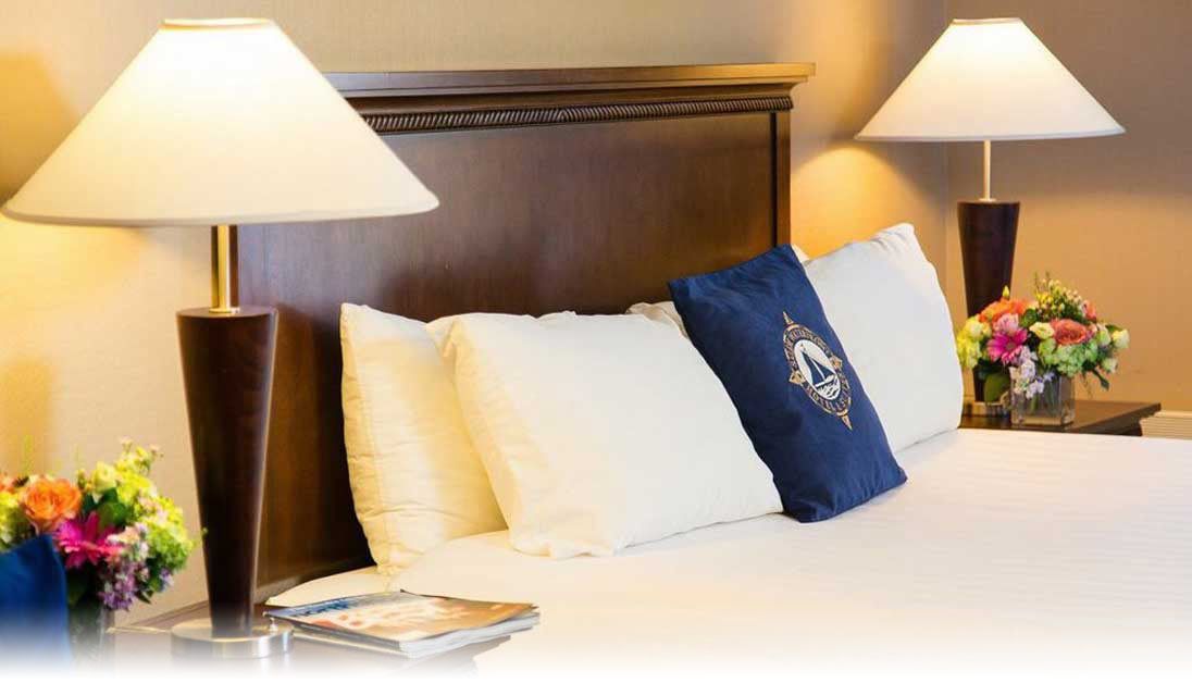 A hotel room with a neatly made bed, two bedside lamps, a floral arrangement, and a magazine on the nightstand.